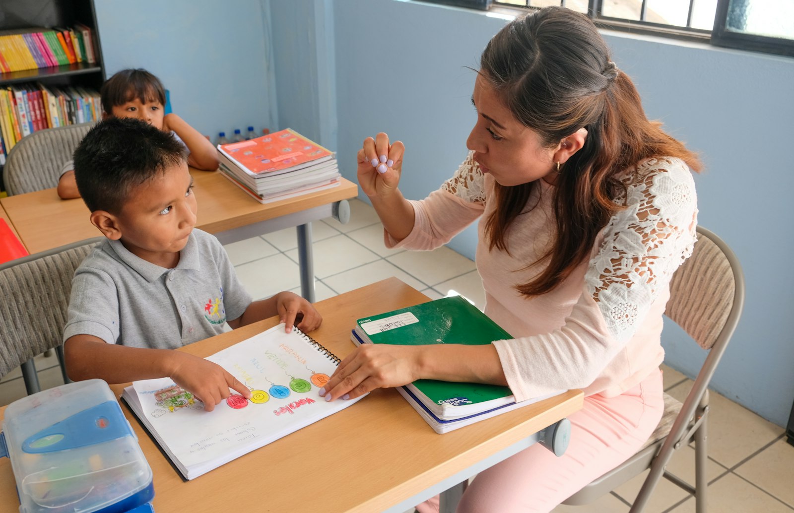 Campaña de admisiones 2027-2028: calendario mes a mes para colegios en México 2 Maestra explicando un cuaderno de trabajo a un alumno en un salón de clases en México